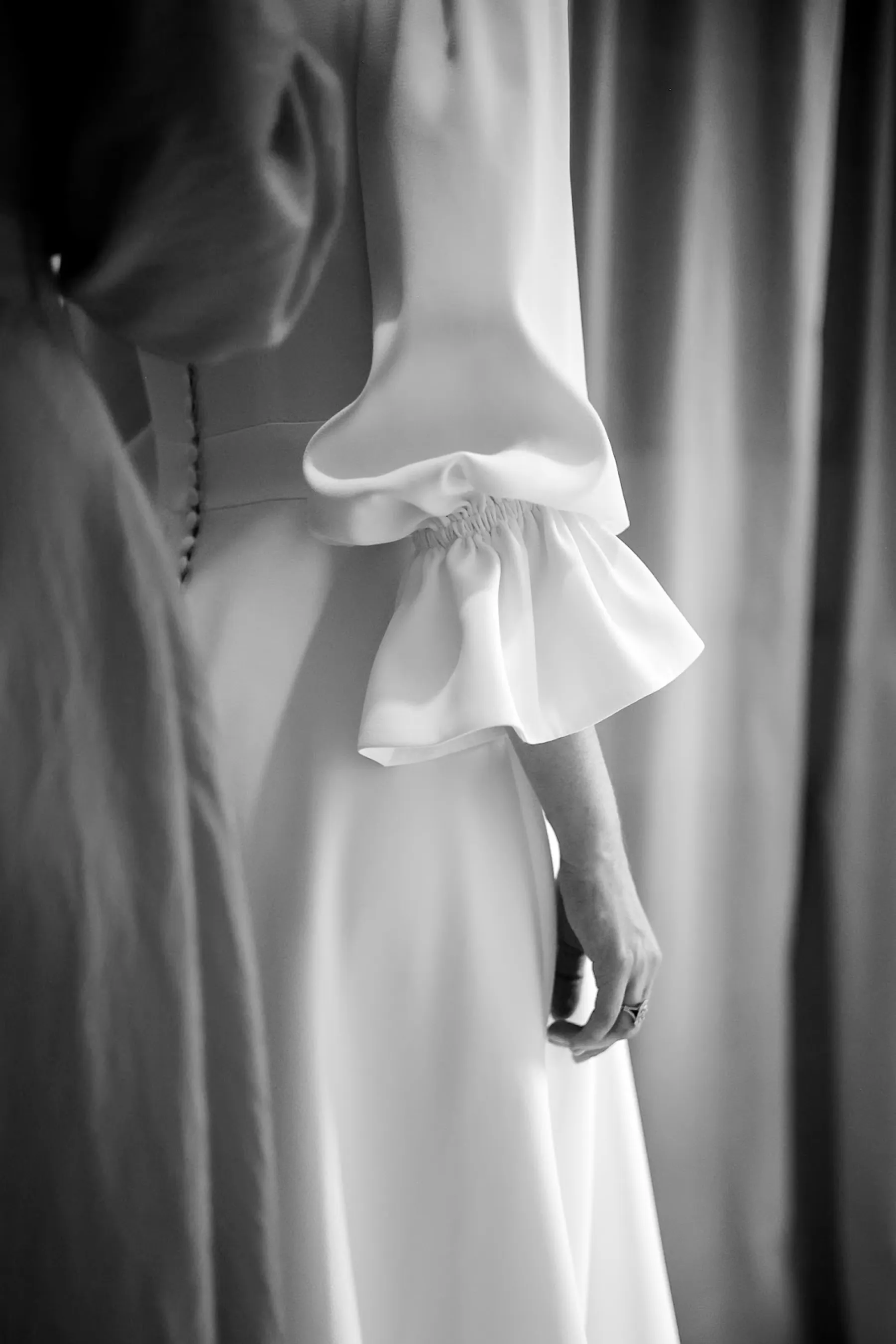 Détail en noir et blanc d'une manche bouffante à poignet volanté de la robe de mariée, dos boutonné