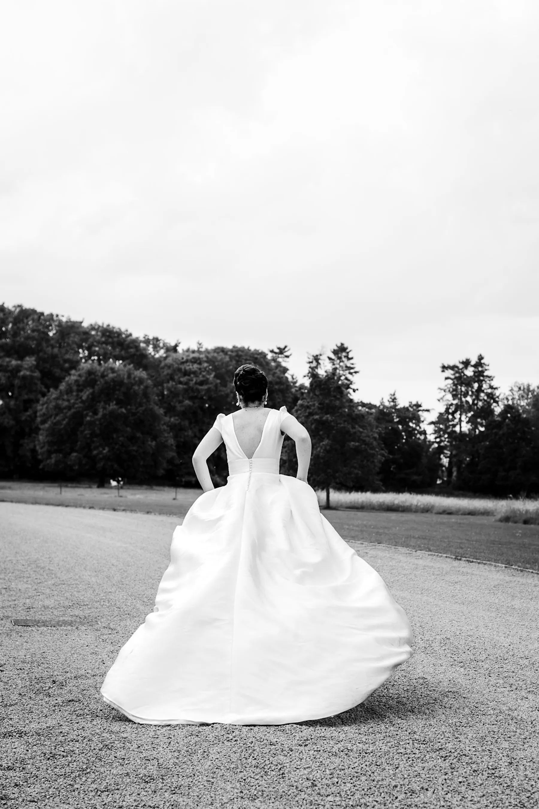 Mariée de dos dans un parc, jupe ample en satin qui virevolte, dos en V, photo en noir et blanc