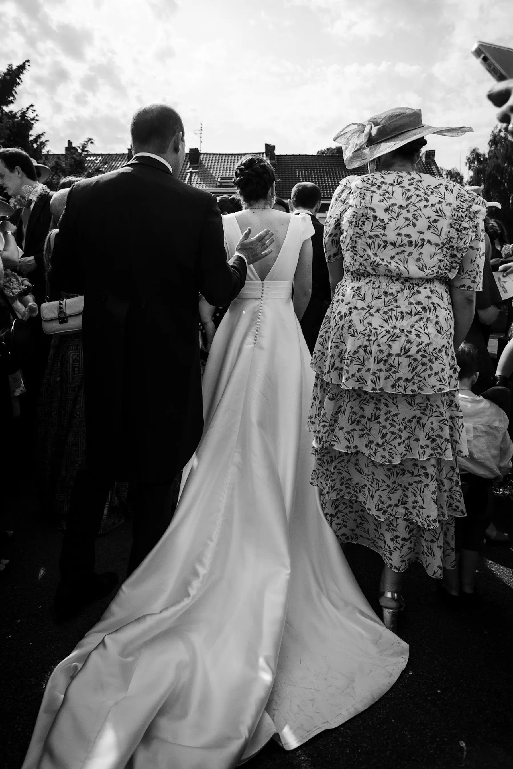 Longue traîne en satin et dos en V boutonné d'une robe de mariée au milieu des invités, en noir et blanc