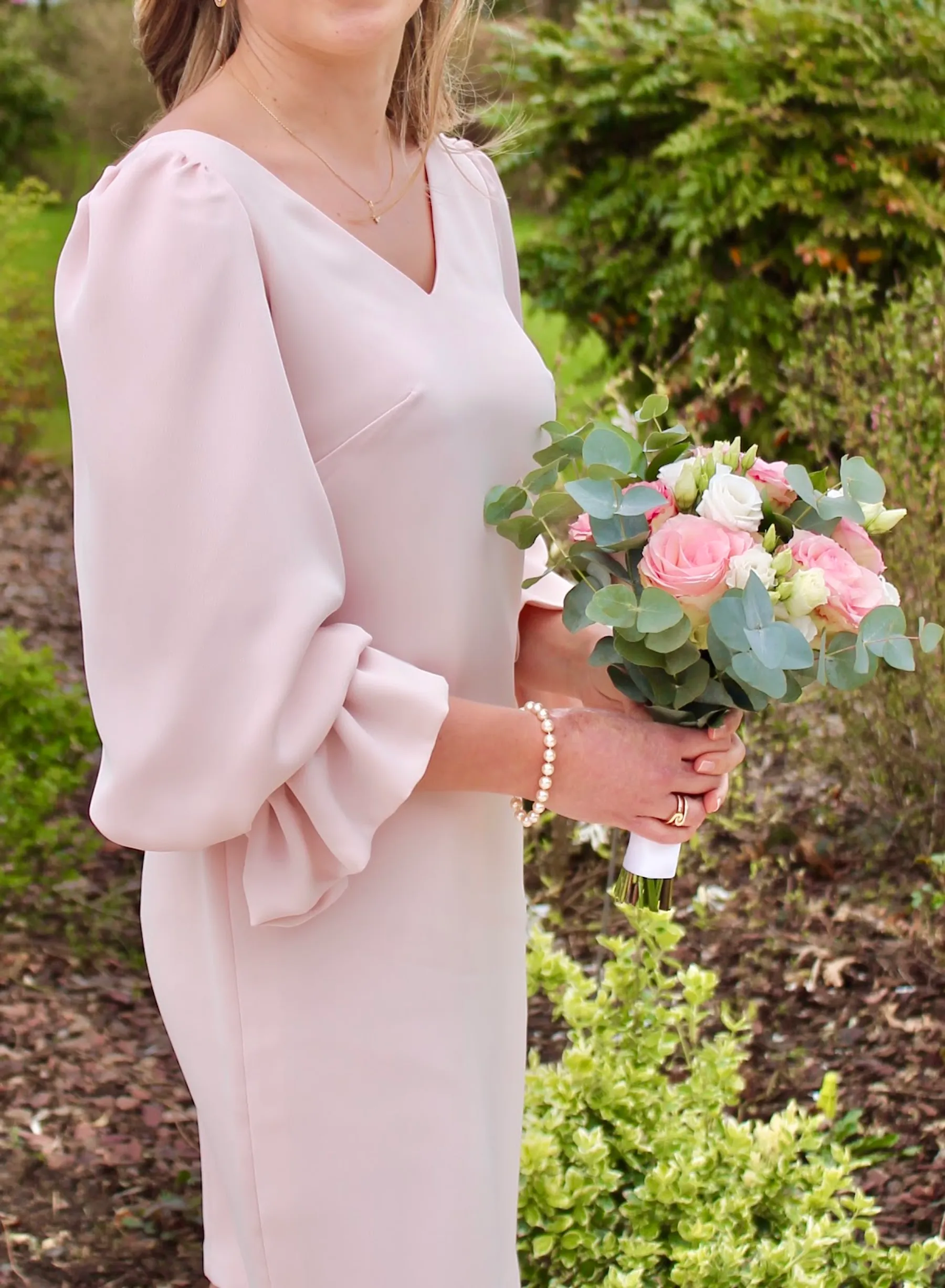 Détail du col V, de l'épaule et de la manche bouffante de la robe rose poudré, avec un bouquet de roses et d'eucalyptus