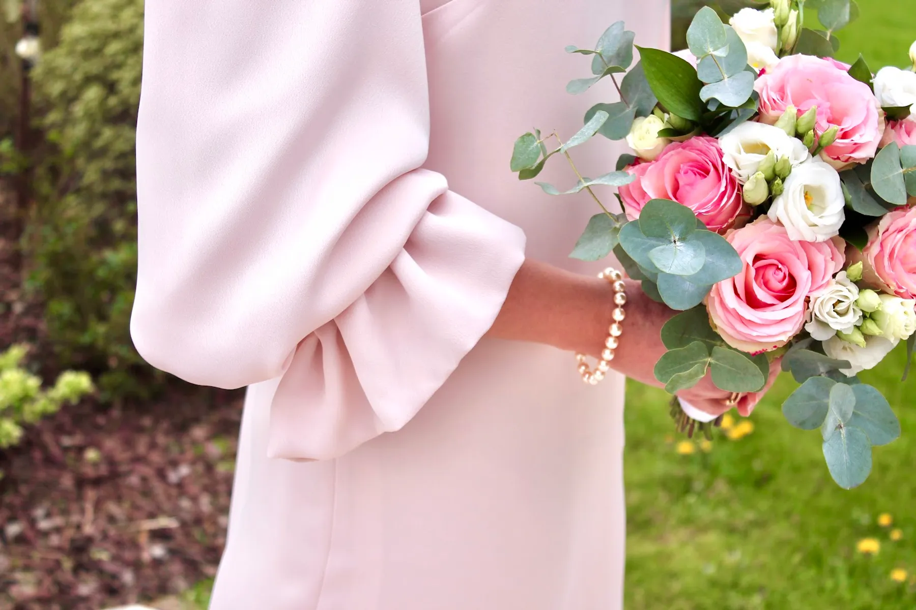 Gros plan sur la manche à poignet volanté d'une robe d'invitée rose poudré, bouquet de roses et d'eucalyptus