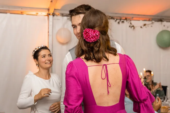 Éléonore de dos près de la mariée, robe d'invitée fuchsia au dos ouvert avec un lien noué, manches bouffantes, fleur dans les cheveux