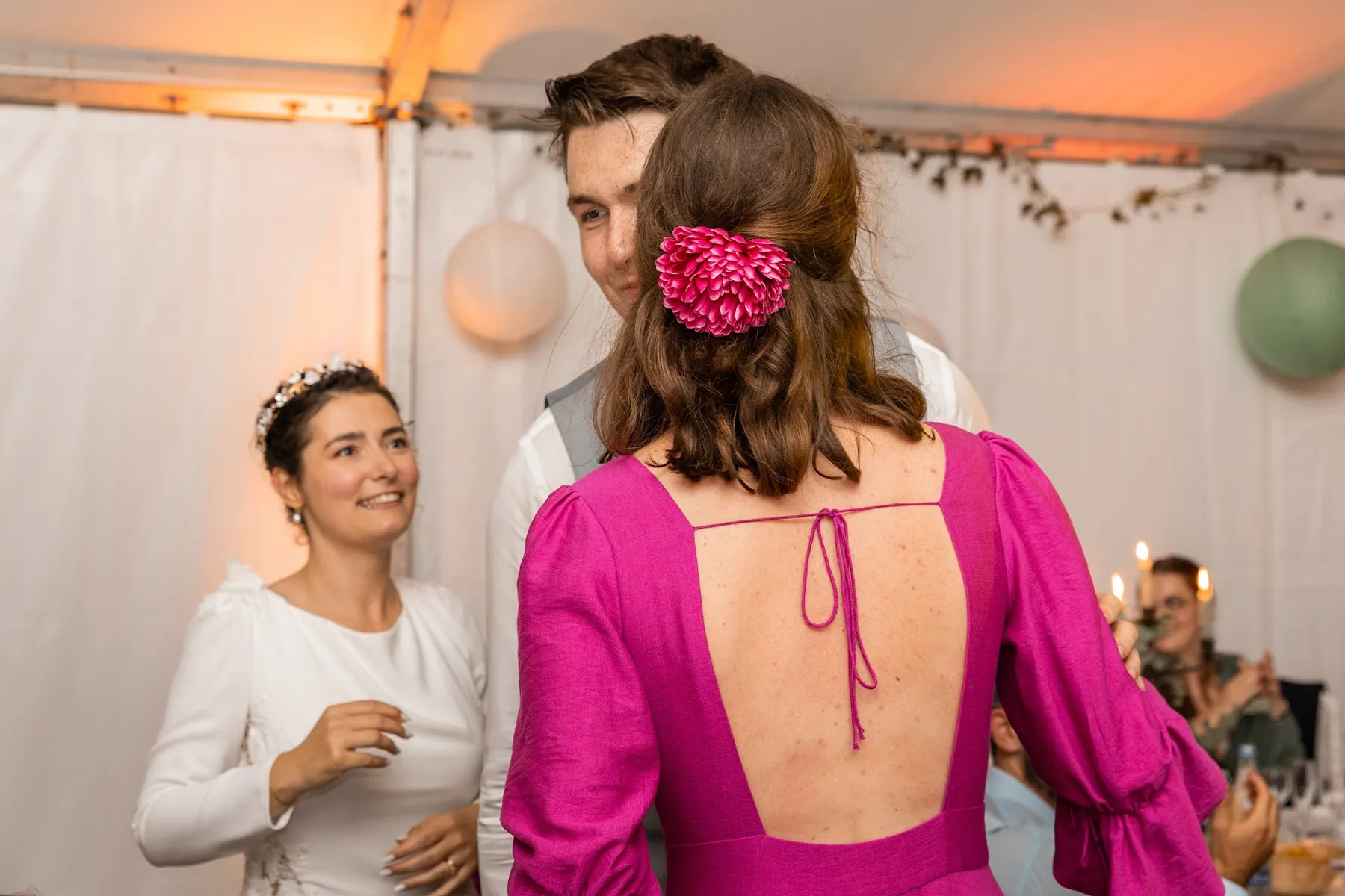Éléonore de dos près de la mariée, robe d'invitée fuchsia au dos ouvert avec un lien noué, manches bouffantes, fleur dans les cheveux