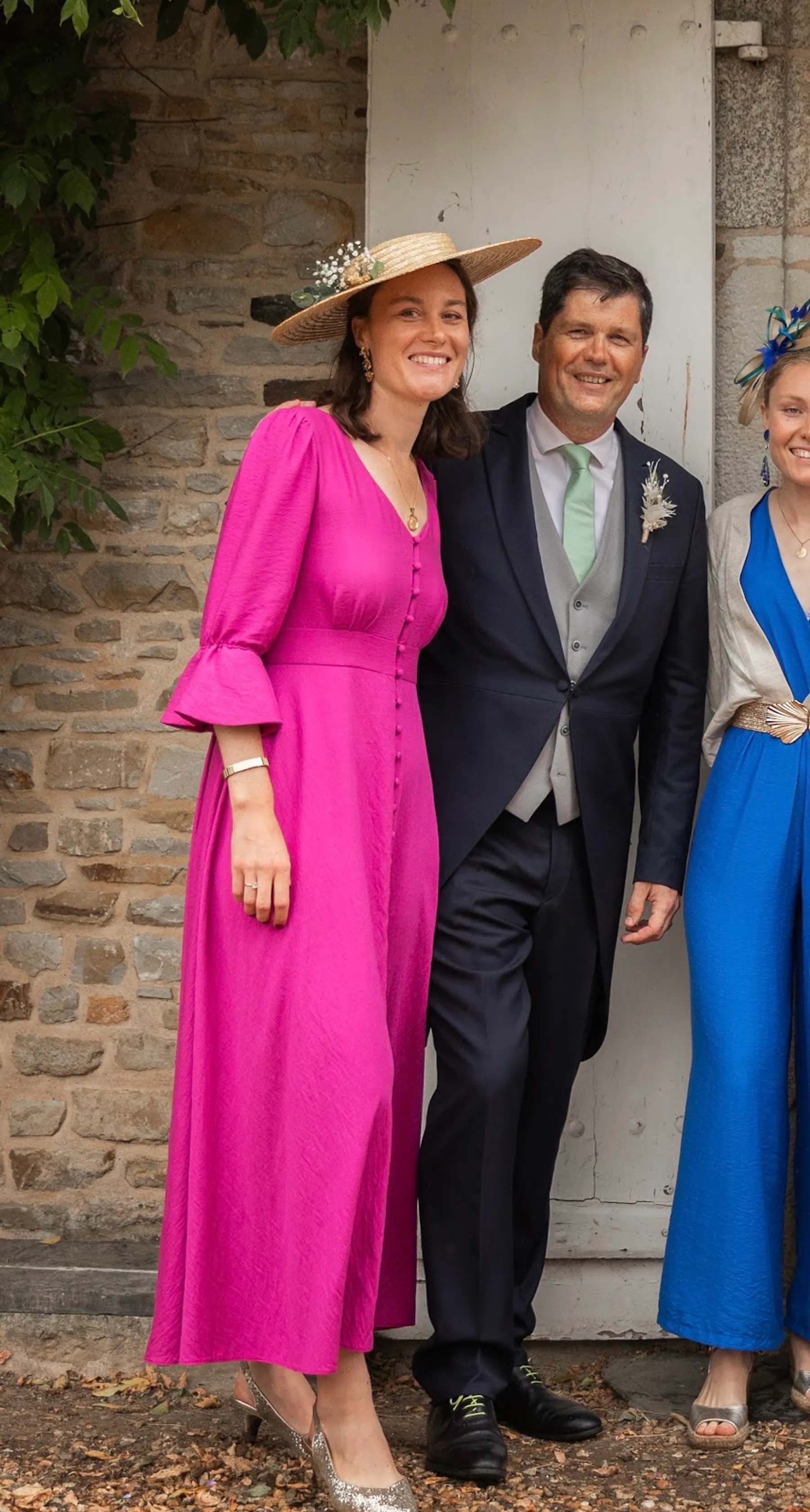Éléonore en longue robe fuchsia boutonnée sur le devant, manches à volants et chapeau de paille, près d'un invité en costume