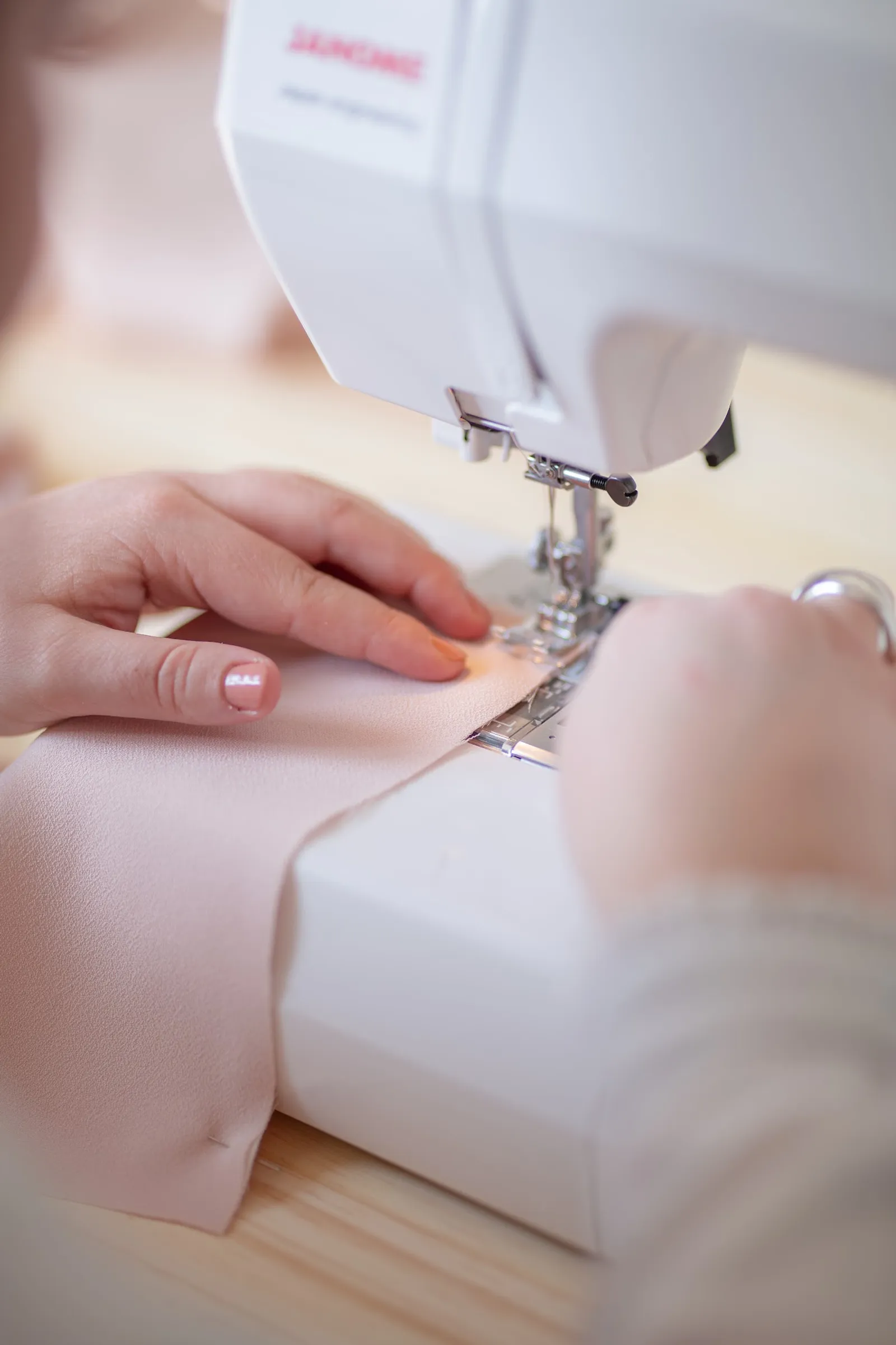 Gros plan sur des mains guidant un tissu sous l'aiguille d'une machine à coudre, à l'Atelier d'Hermine.