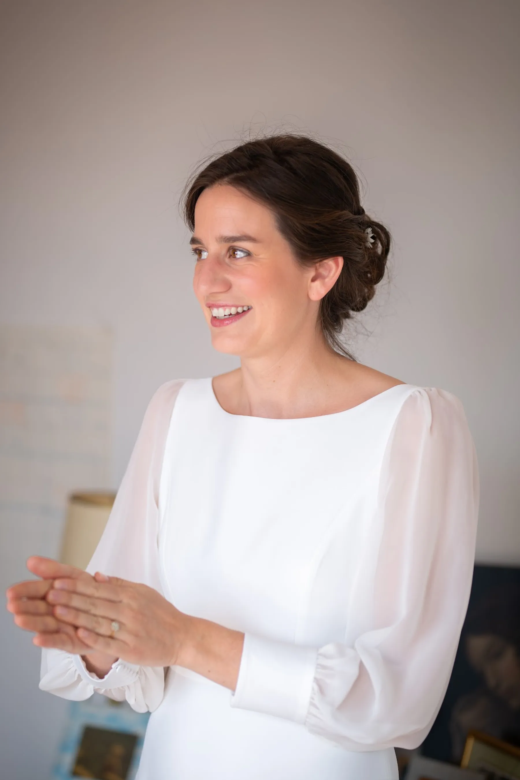 Hosanne souriante en robe de mariée à col bateau et manches en mousseline transparente, mains jointes