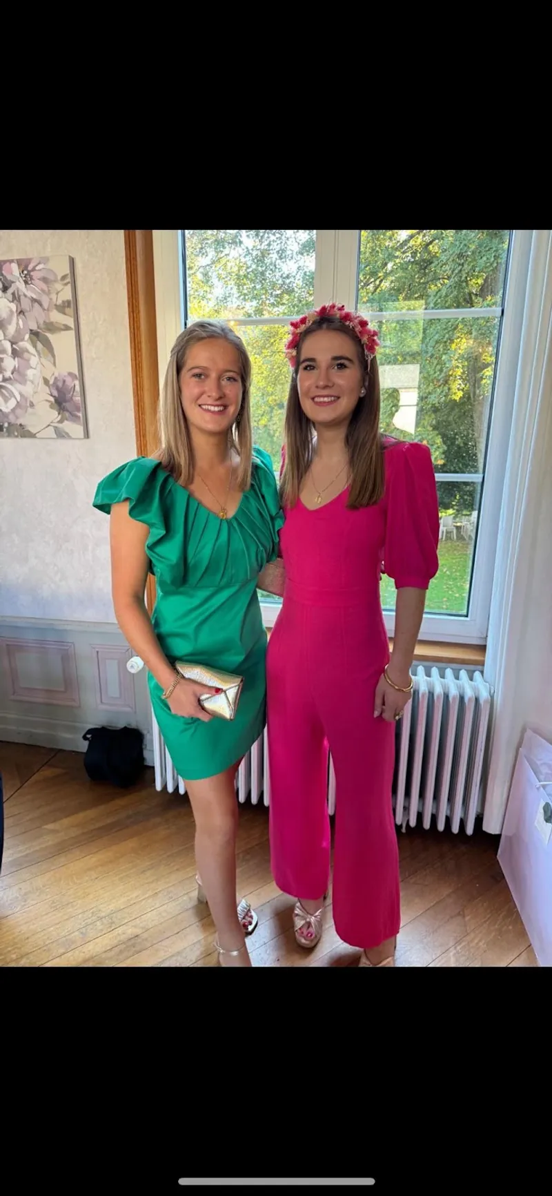 Jeanne, à droite, en combinaison-pantalon rose fuchsia à manches bouffantes et couronne de fleurs, à côté d'une amie en robe verte