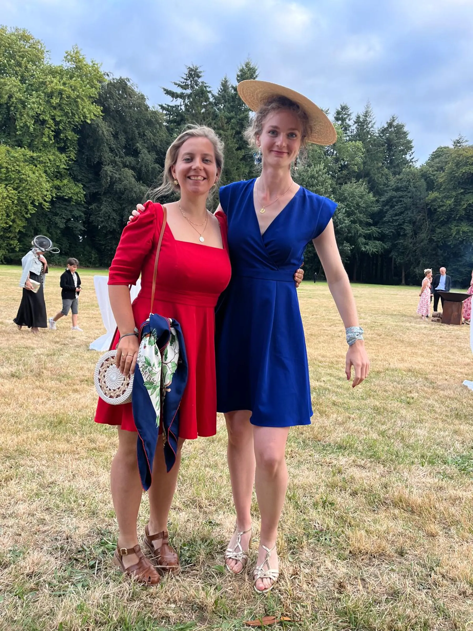 Sarah, en robe rouge évasée à manches courtes bouffantes, avec une amie en robe bleue dans un champ