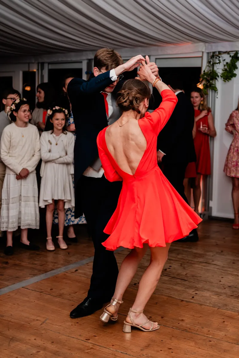 Tiphaine danse en robe rouge orangé à dos plongeant en V et jupe évasée qui tourne, sous une tente de réception